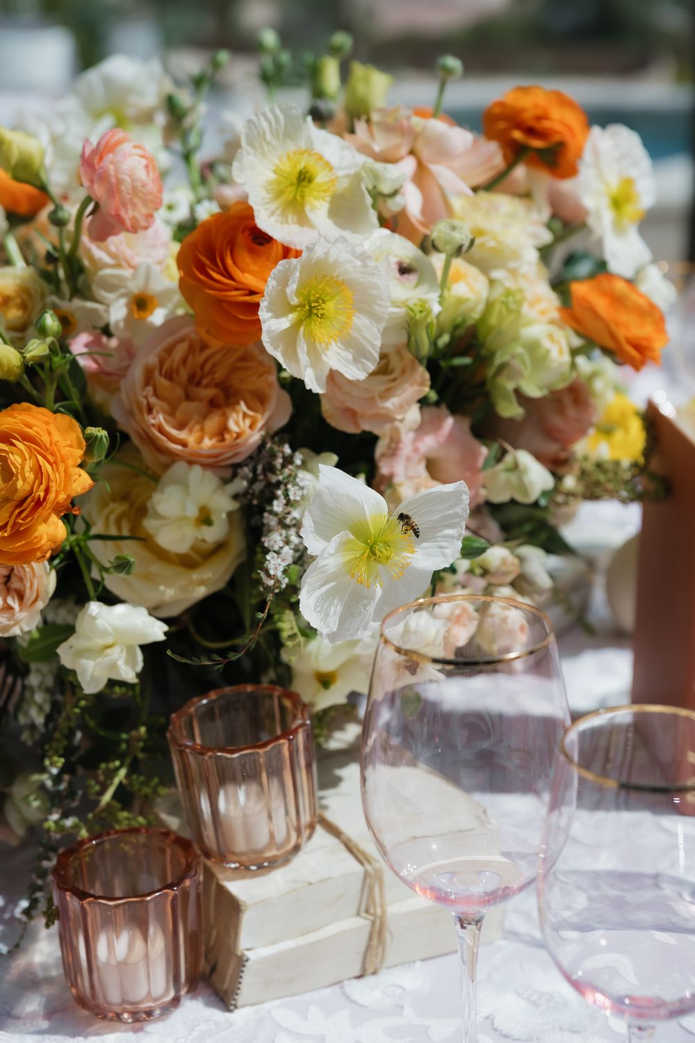 Elegant table setting with pink and orange floral centerpiece featuring ranunculus and daisies alongside blush glassware.