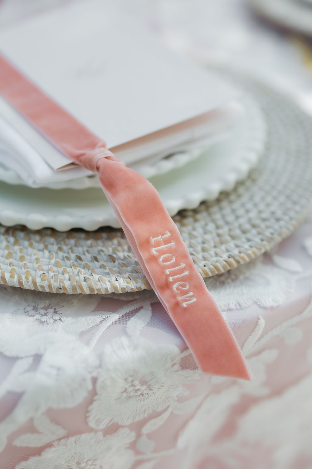 Pink velvet ribbon place cards with elegant calligraphy displayed on textured lace fabric.