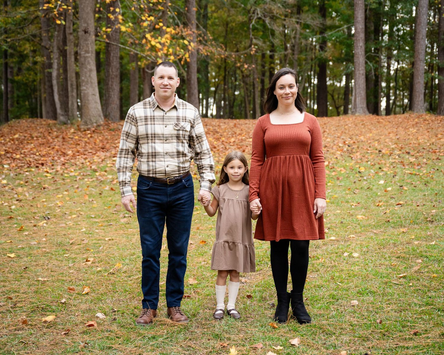 Autumn family portrait session in wooded park with fallen leaves.