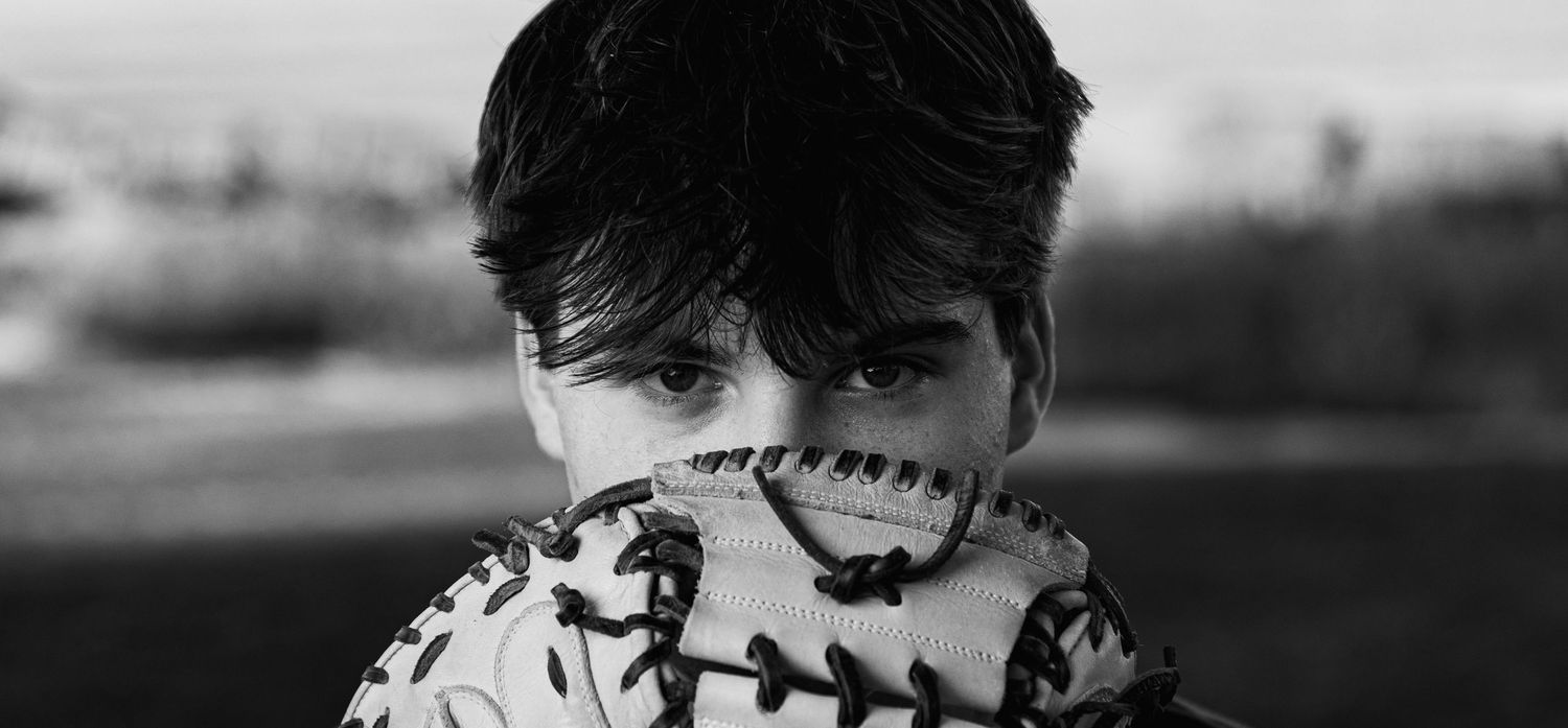 Black and white image of a high school senior baseball player holding his mitt over his face.