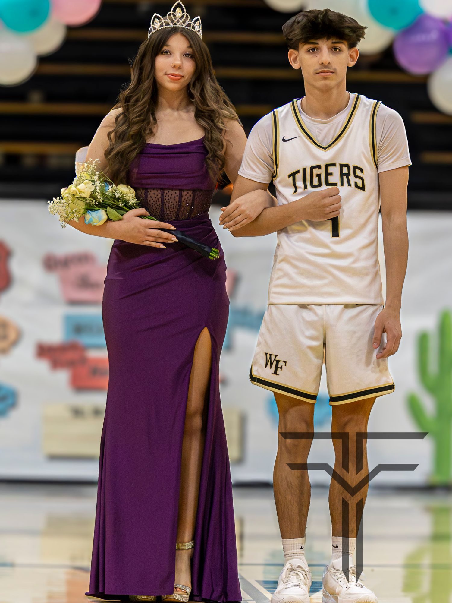 Young woman in purple gown with tiara holds bouquet beside male Tigers basketball player number 1 at school homecoming ceremony.