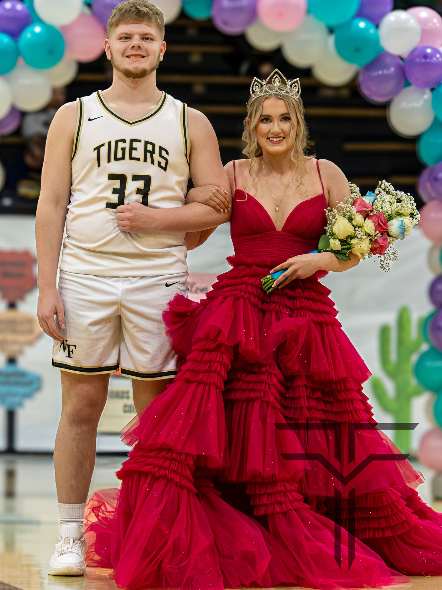 A Tigers basketball player in jersey 33 escorts a girl in a red ruffled gown with a crown at a school ceremony.