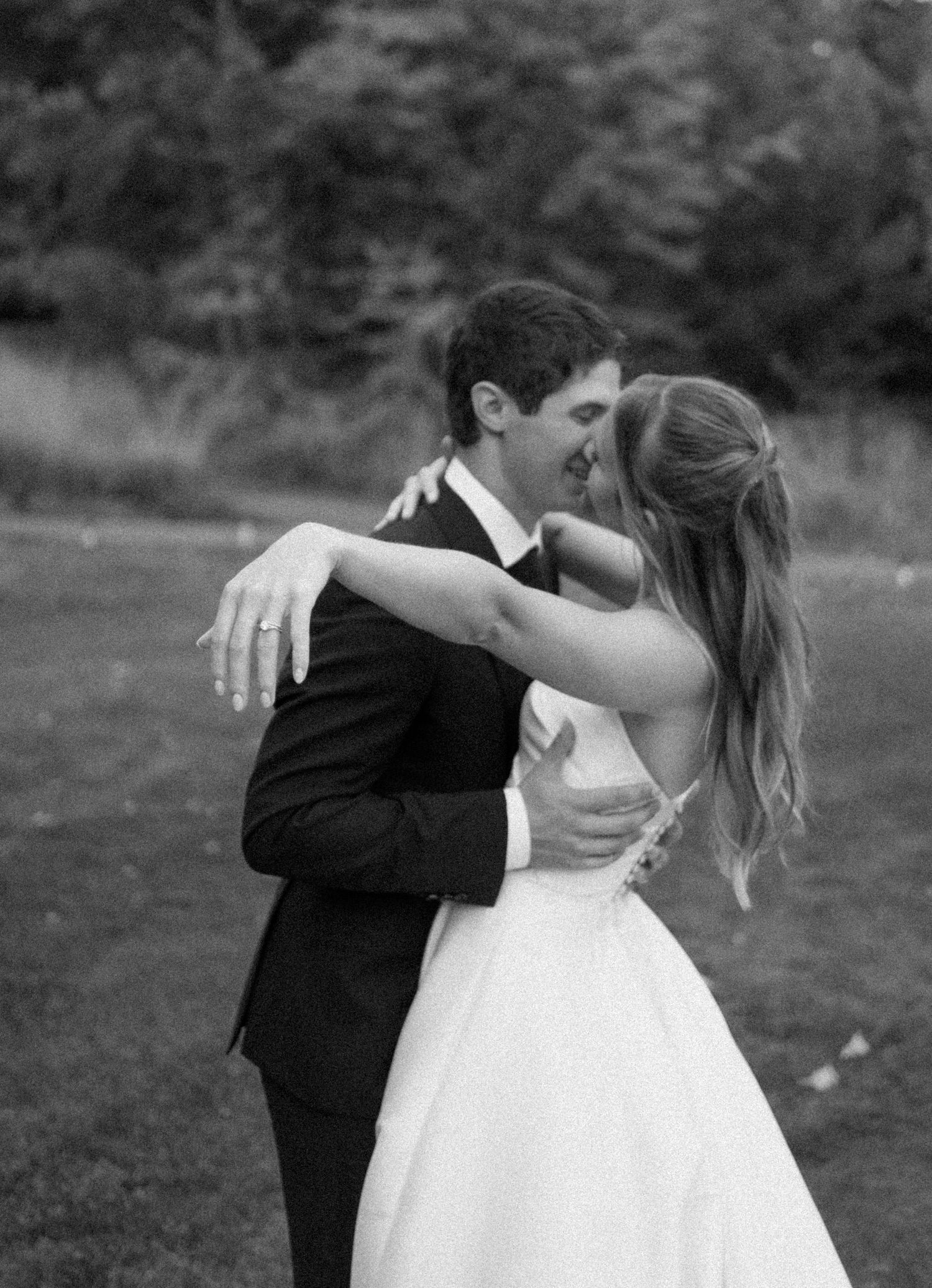 A romantic black and white wedding photo shows a couple in formal attire dipping during a dance pose outdoors-Alexis Anne Photography