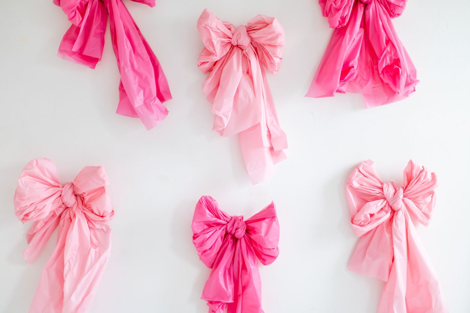 Pink and hot pink tissue paper bows arranged in a decorative pattern against a white background.