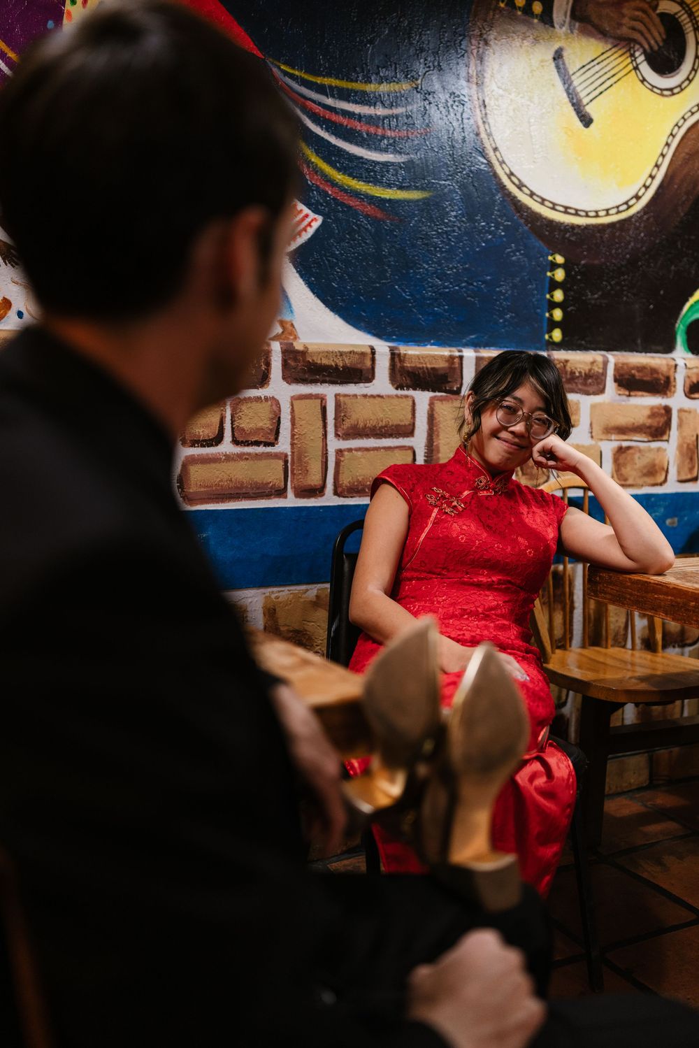 A person in a red dress sits at a rustic wooden table in a dimly lit restaurant with decorative guitars on the wall.