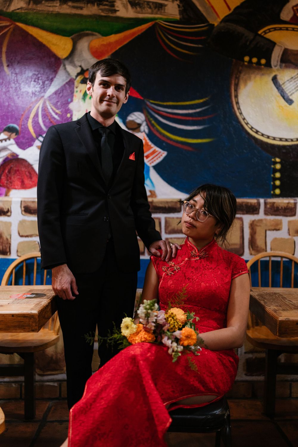 A couple in formal attire shares intimate moments at a restaurant with colorful wall murals and decor.