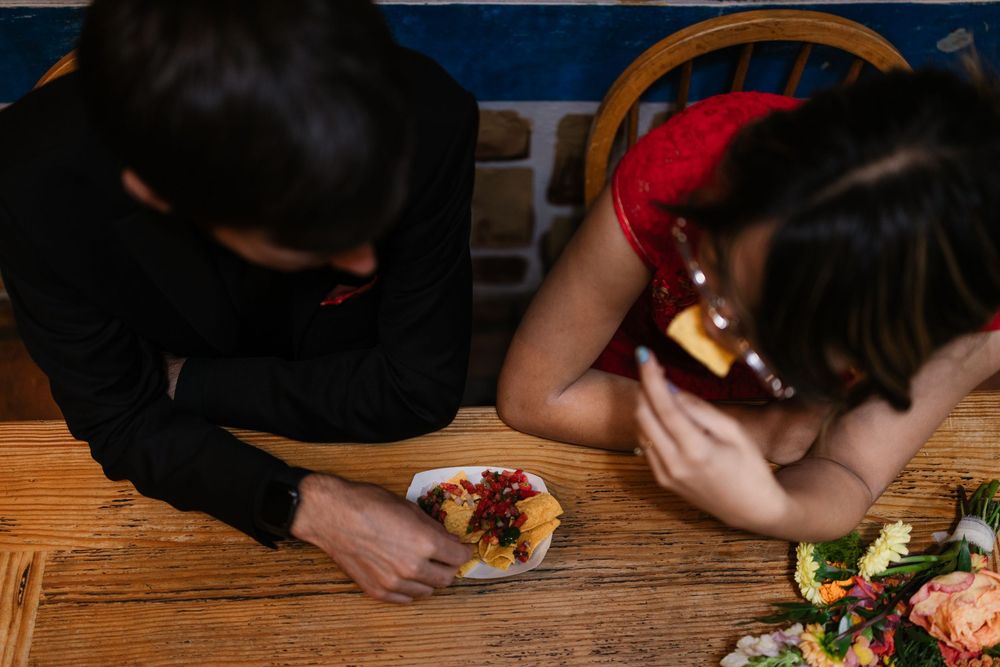 A person holds a colorful sandwich filled with fresh ingredients on a wooden table.
