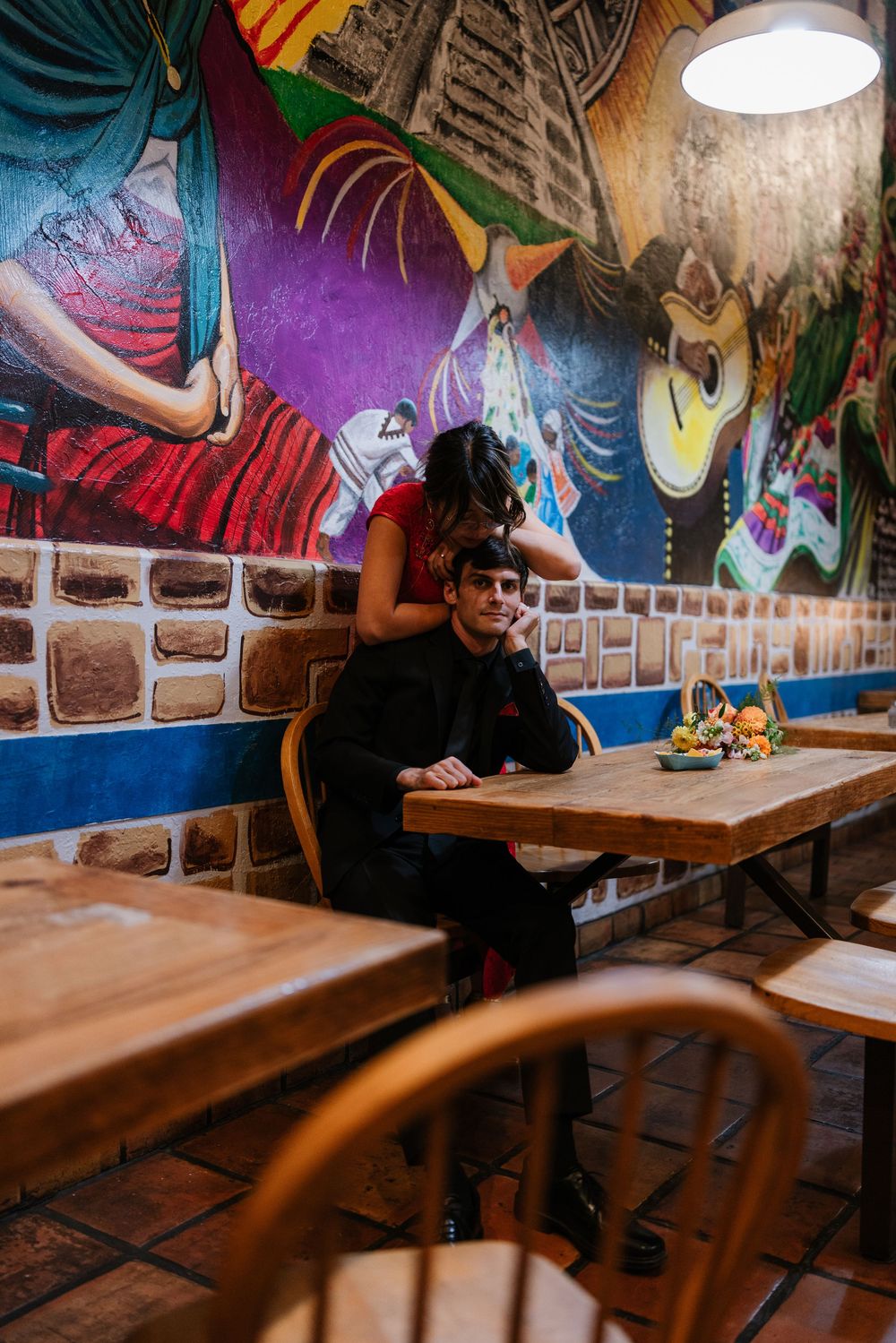Person sitting at wooden table in colorful restaurant with graffiti-style murals on brick walls and pendant lighting.