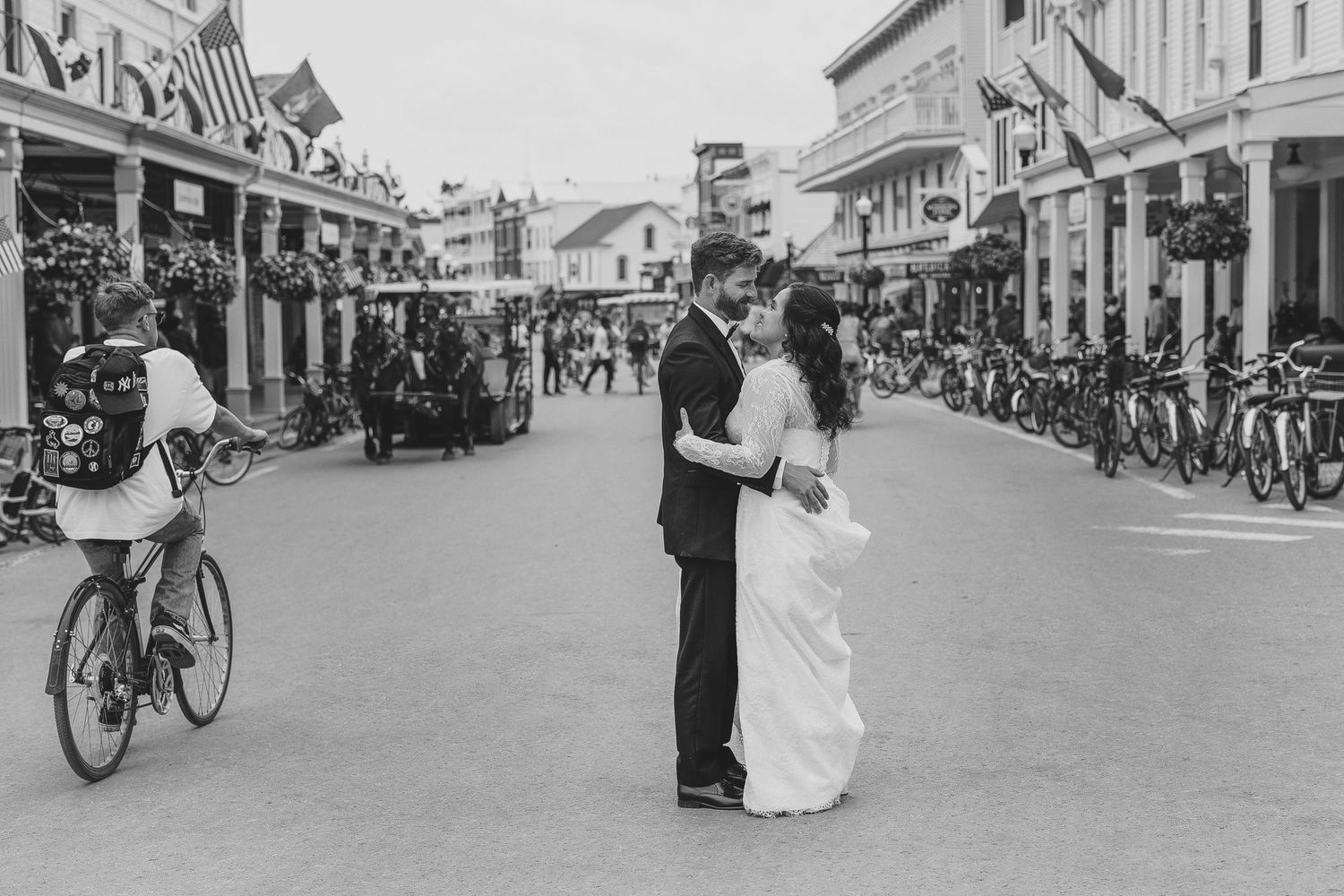 A black and white street scene shows a couple embracing on Mackinac Island's Main Street with storefronts and a cyclist visible.