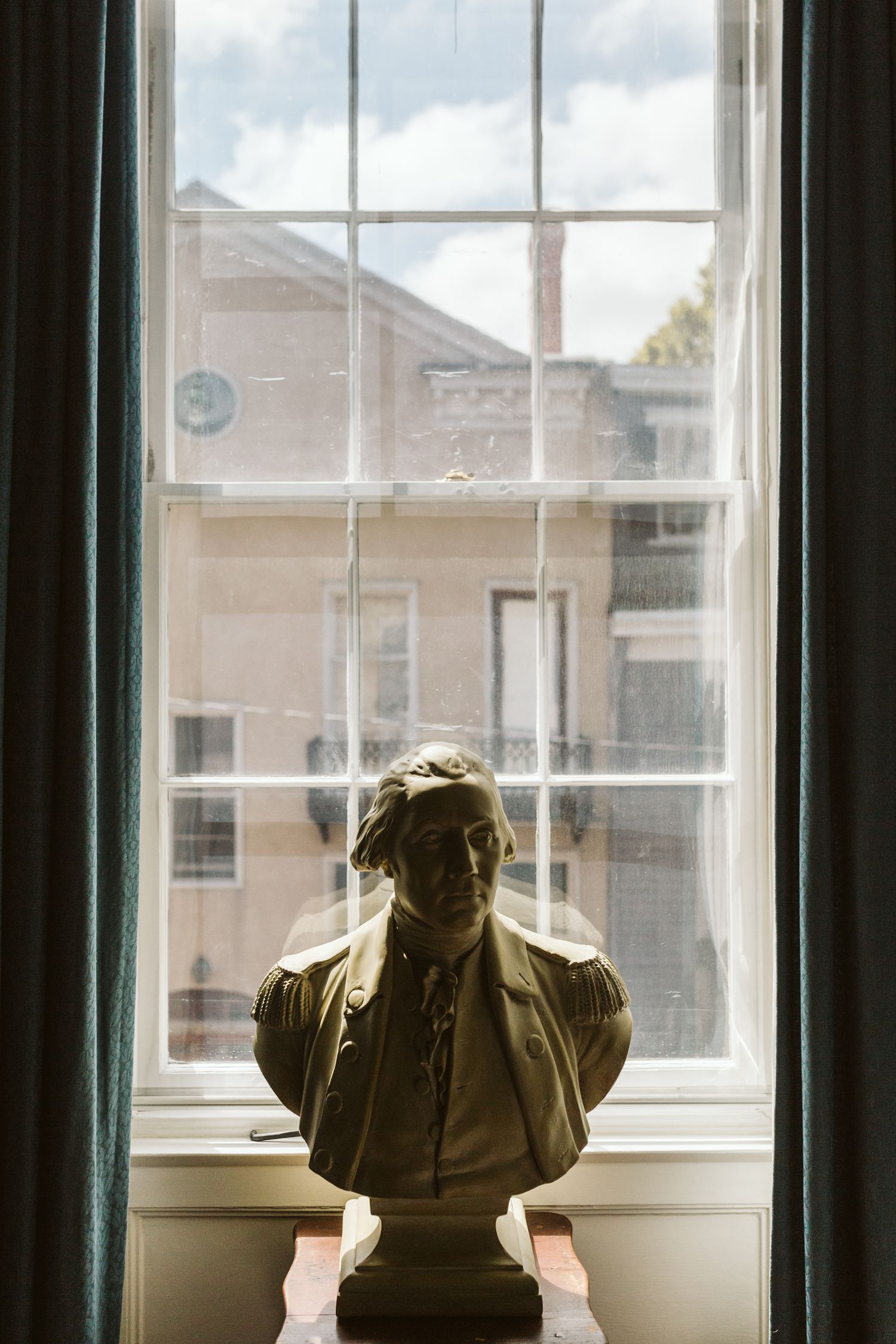A silhouetted bust sculpture sits on a windowsill with natural light streaming through paned windows.