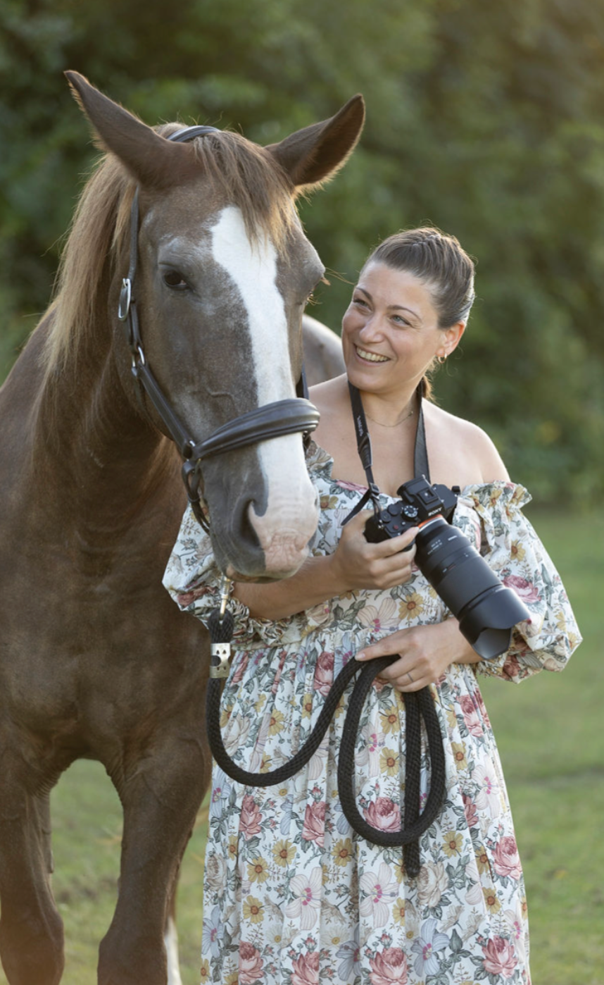A person in a floral dress shares a tender moment with a brown horse in an outdoor setting.