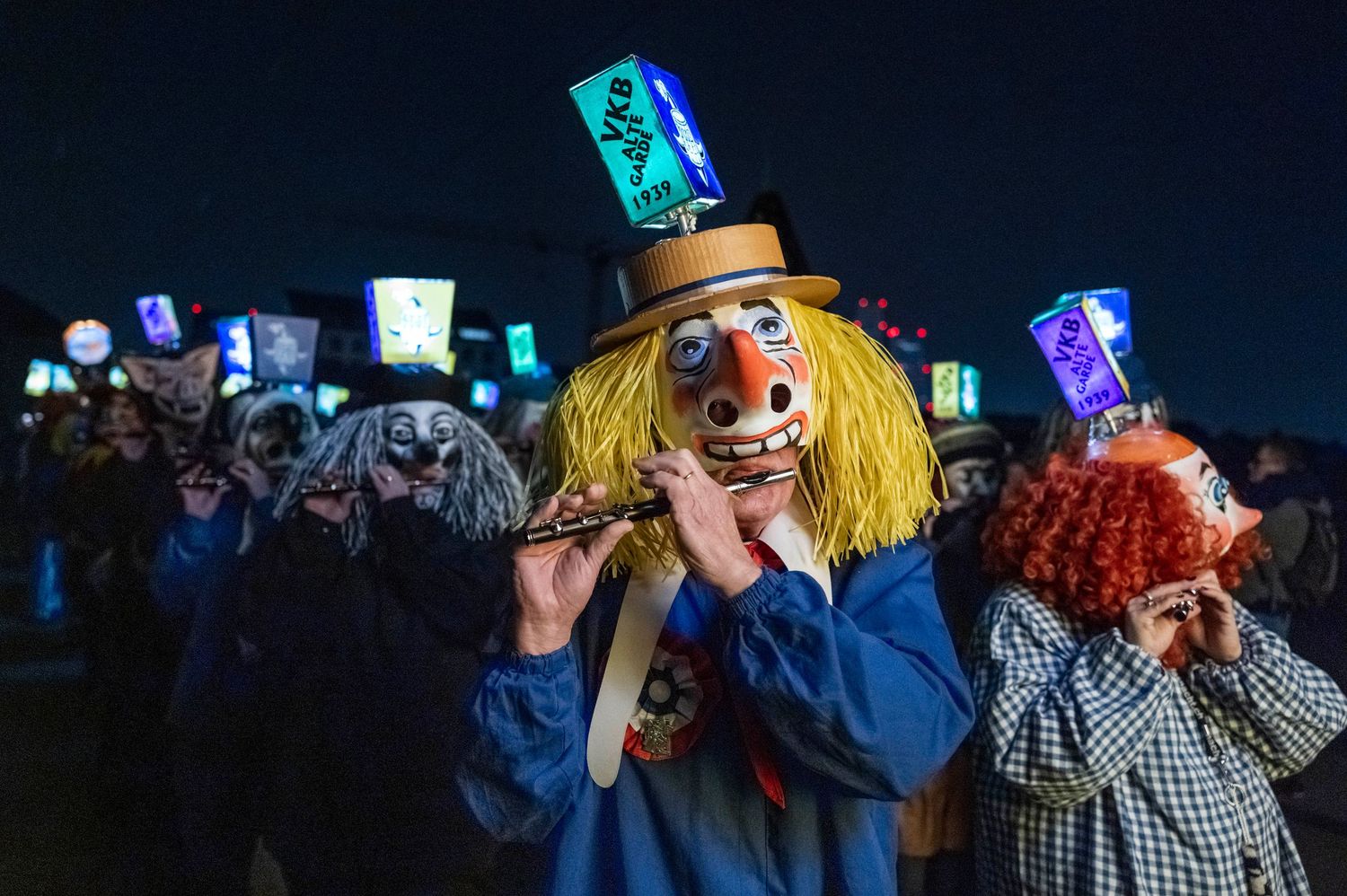 Festival revelers with glowing lights and costumes dance at nighttime celebration.