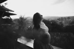 Silhouette of pregnant woman standing on balcony during sunset.