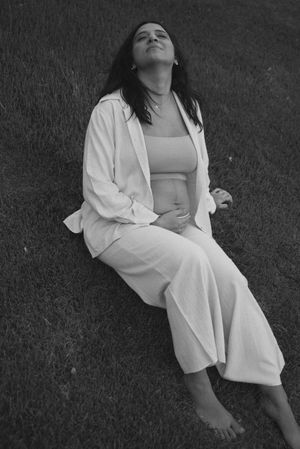 Monochrome photo of pregnant woman relaxing on ground in flowing white outfit.