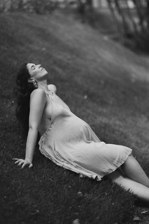 A person in a white dress lies peacefully on grass in a black and white artistic photograph.