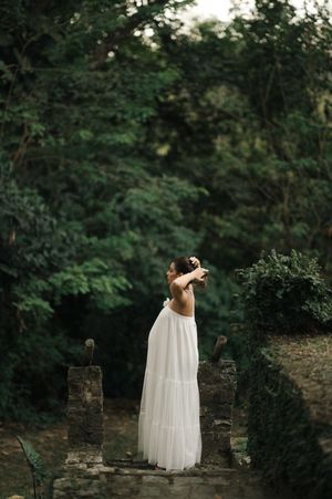 A romantic white dress stands out against lush greenery in a moody forest setting at dusk.