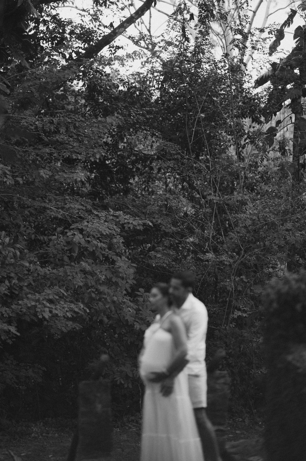 A romantic black and white photo series shows a couple embracing in front of trees and foliage.