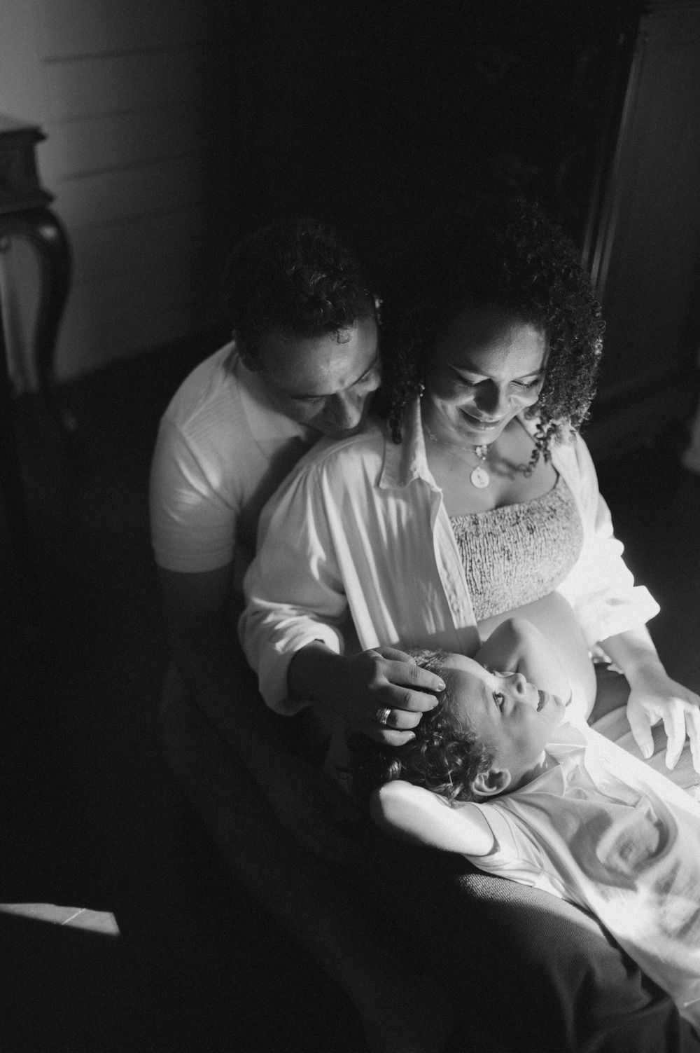 A tender black and white photograph of parents sharing a joyful moment with their baby in an intimate setting.