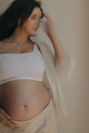 Artistic maternity portrait featuring soft lighting and flowing white fabric.