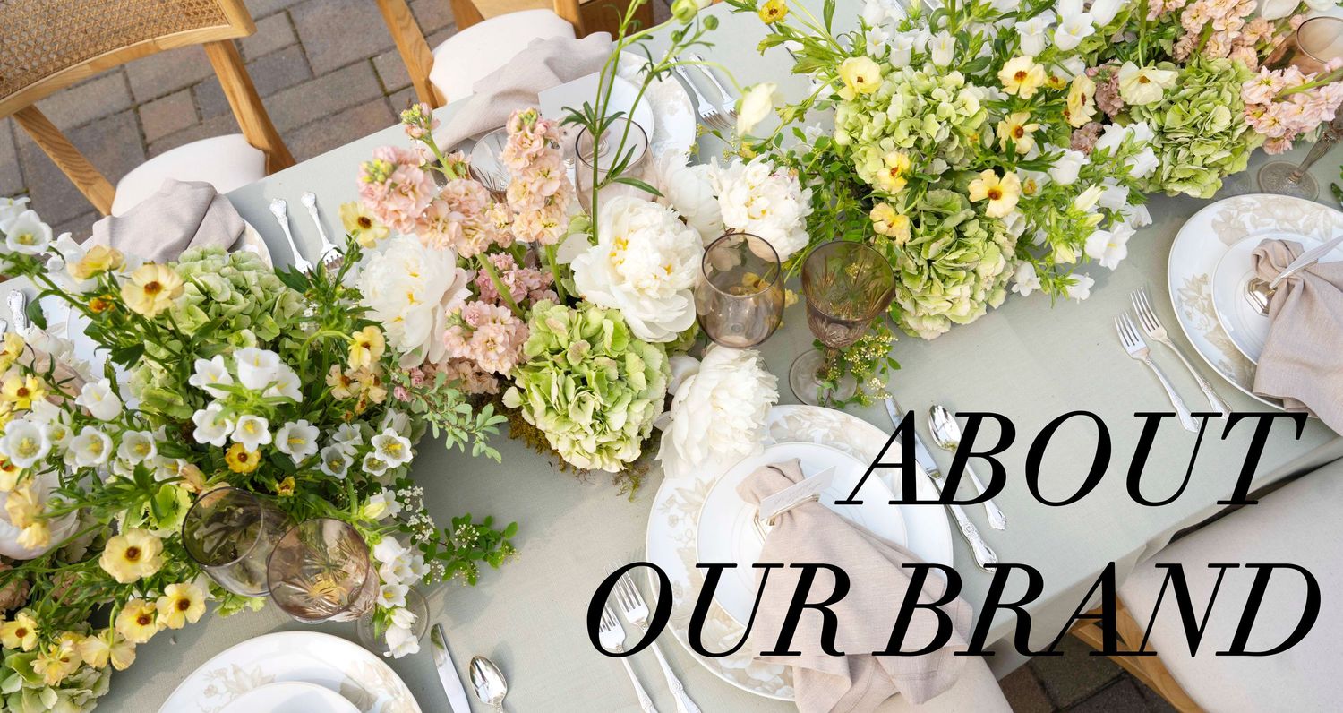 Wedding flatlay with white and green florals, vintage books, ribbons, and delicate styling details on neutral surface.