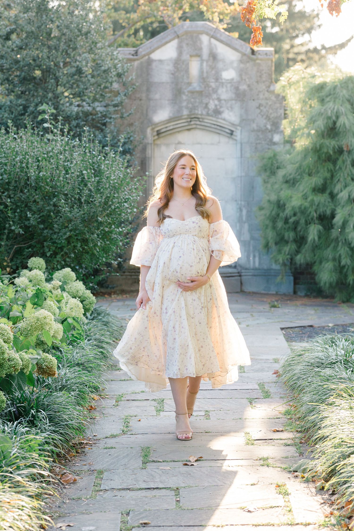 A person in a flowing white lace dress sits outdoors with a basket of baby's breath flowers in a dreamy garden setting.