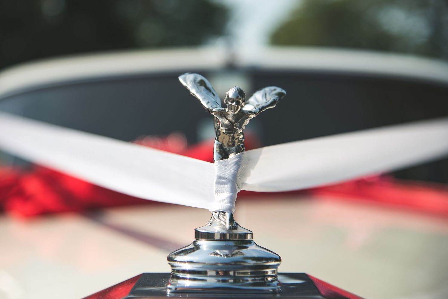 A silver Rolls-Royce hood ornament known as the Spirit of Ecstasy reflects light against a blurred background.