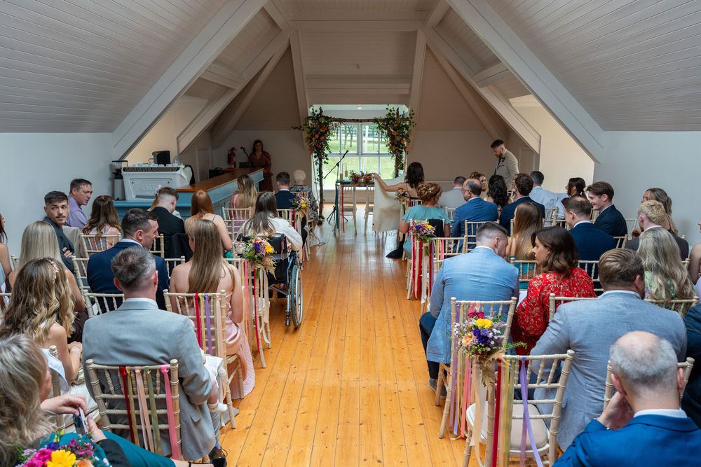 A group of people seated in rows inside a bright attic-style room with wooden floors and white walls during an event.
