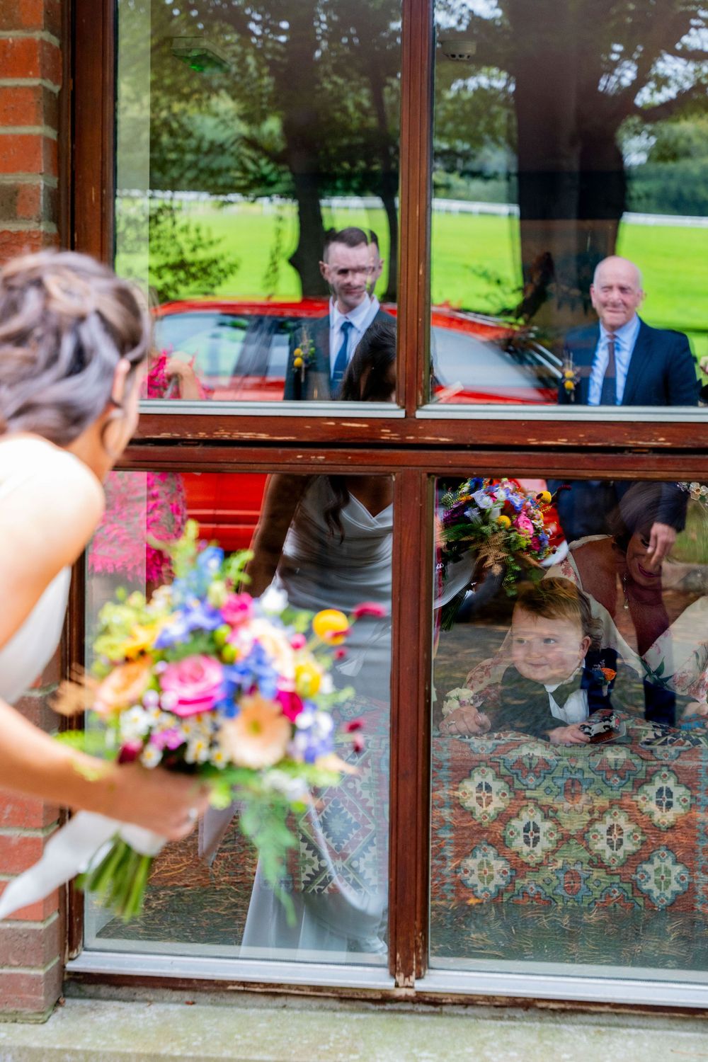 A colorful wedding bouquet held up to a window where people can be seen sitting inside.