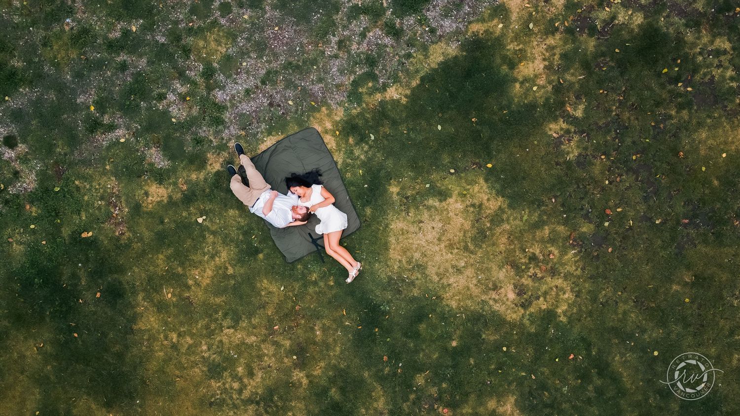Aerial drone shot of a person lying in a grassy field surrounded by nature.