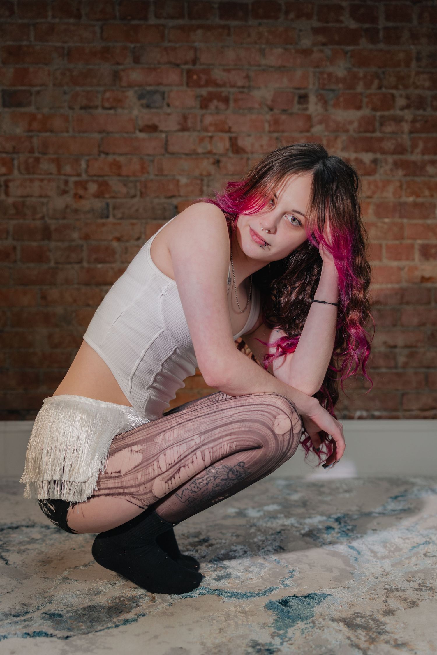 A dancer in white top and stockings performs a dramatic pose sequence against a rustic brick wall background.