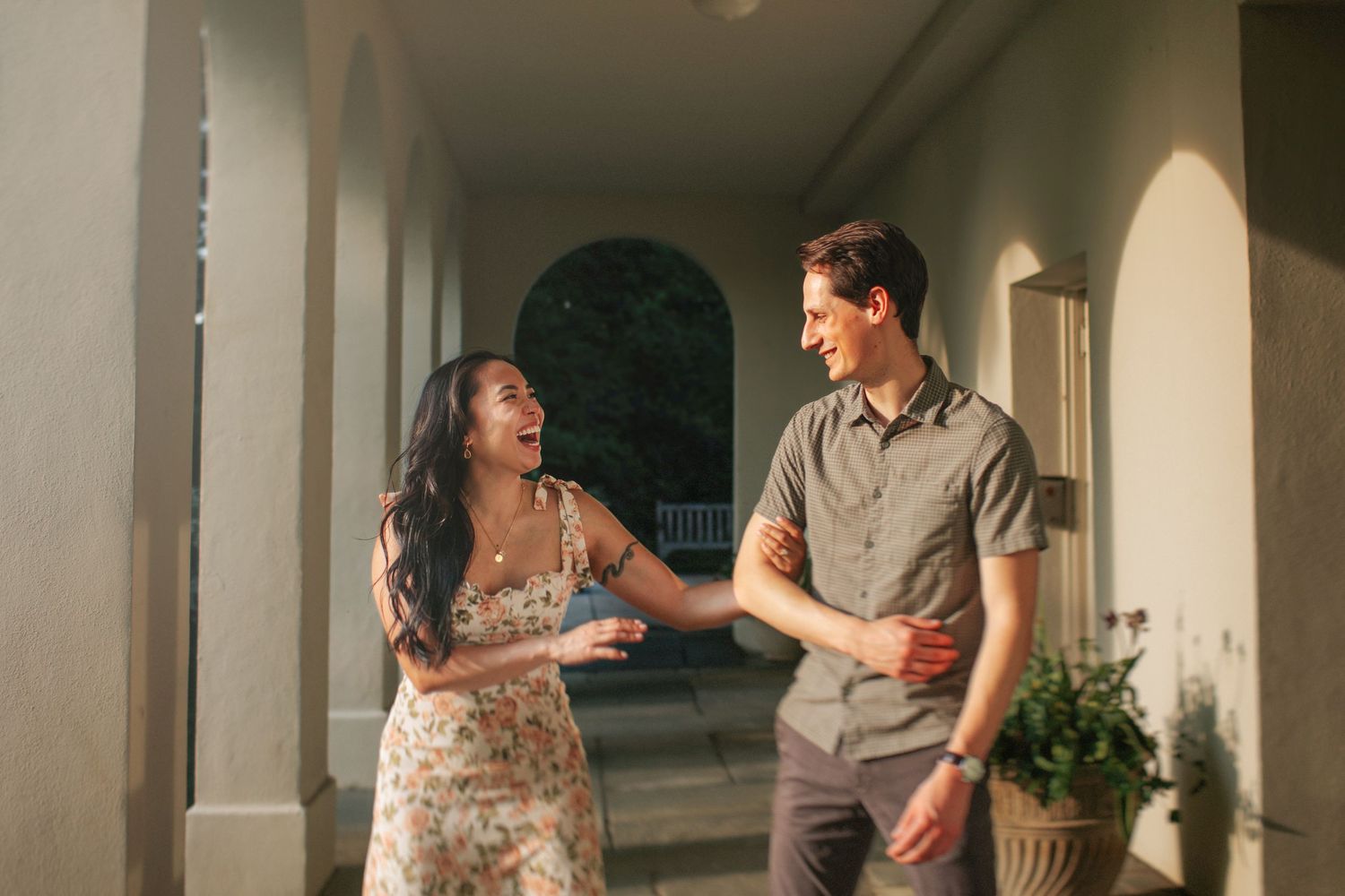 A couple shares a joyful moment while walking together along a covered outdoor porch at sunset.