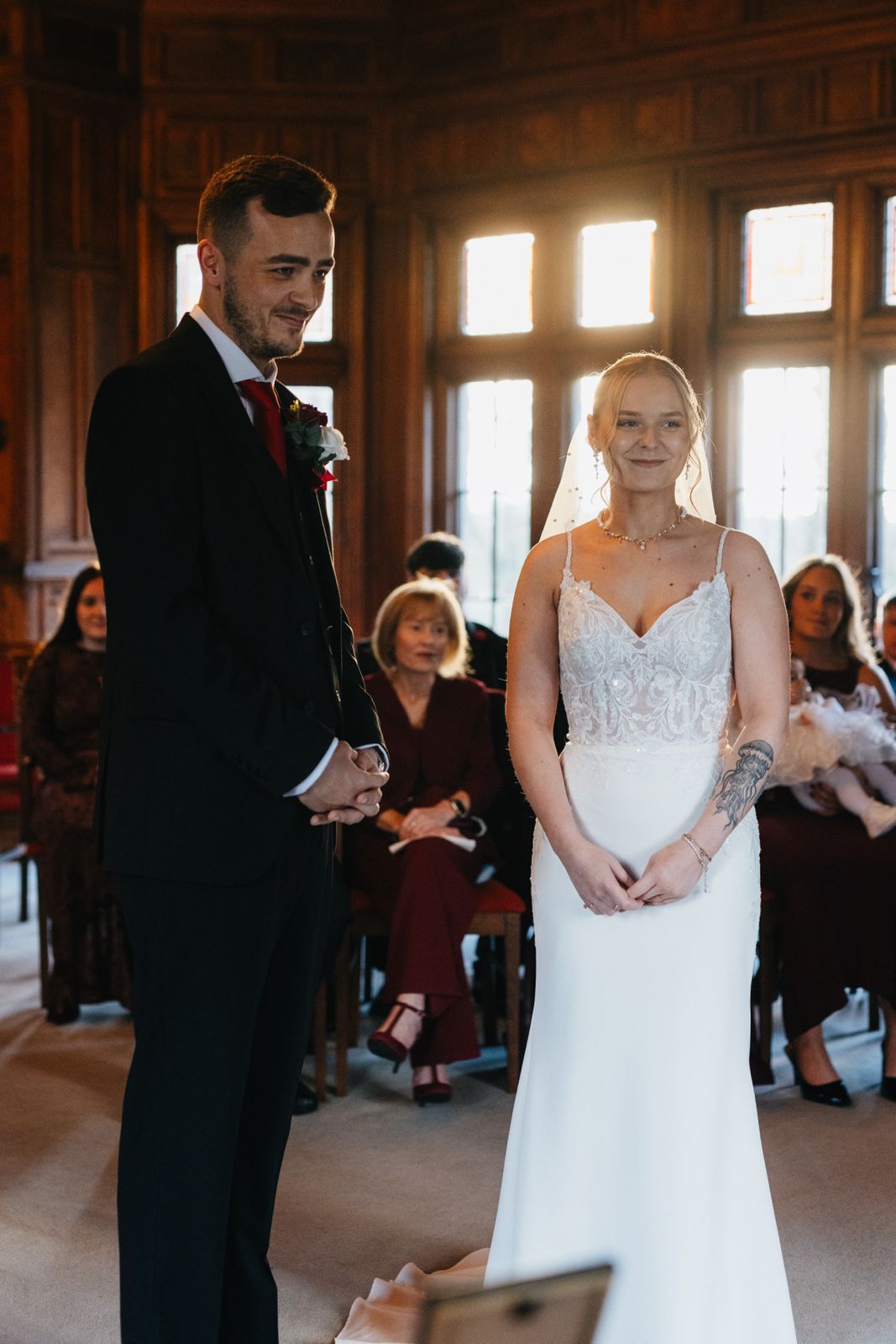 Elegant bride and groom share an intimate first dance moment in a grand wooden ballroom with natural light streaming in.