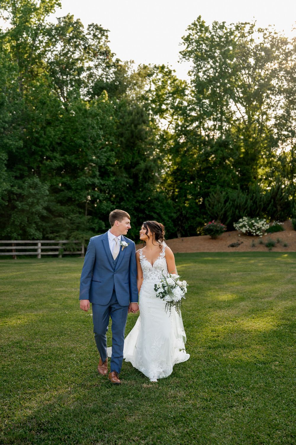 Newlyweds walking hand in hand across sunny lawn at outdoor wedding venue.