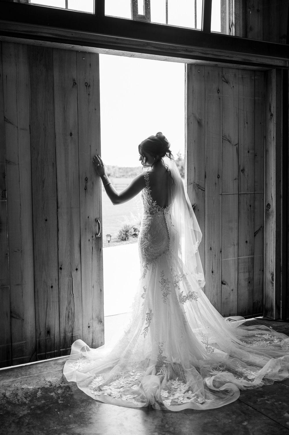 Silhouette of wedding dress against rustic barn windows in black and white.