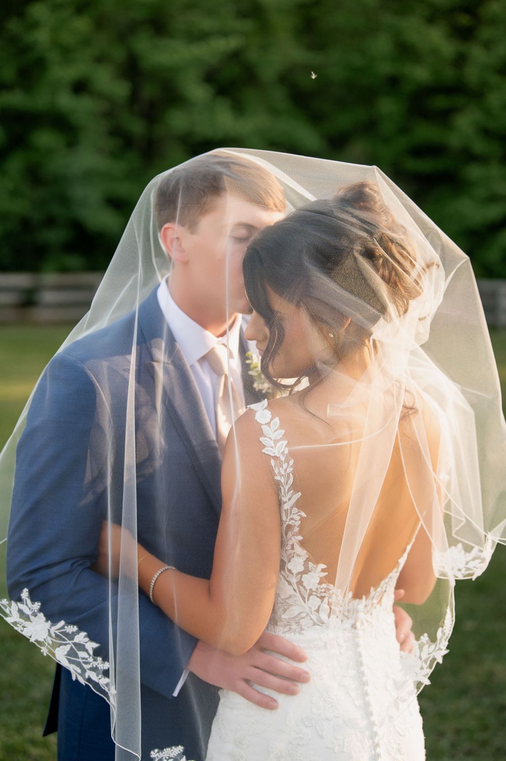 Intimate wedding portrait under a delicate lace veil during golden hour.