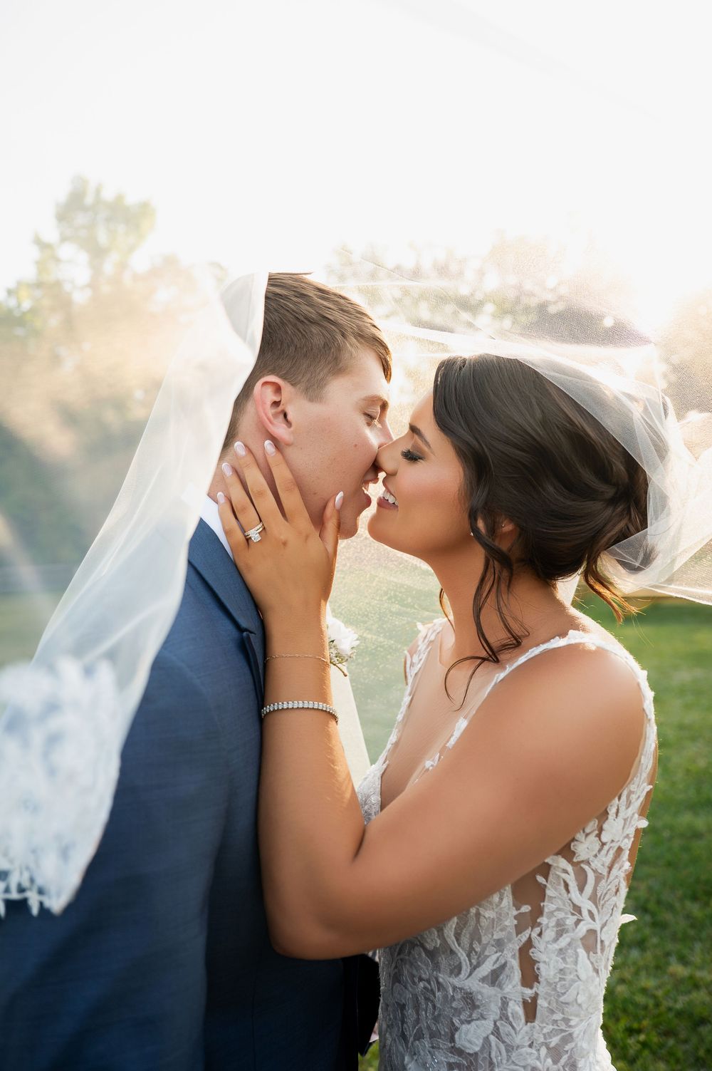 Romantic outdoor wedding portrait with bride in lace dress and groom in navy suit.