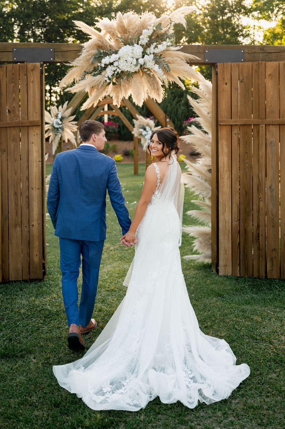 Wedding couple under stunning pampas grass and floral arch in garden setting.