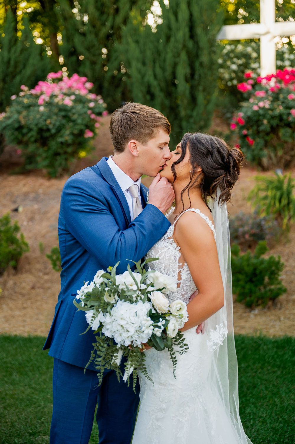 Garden wedding portrait with white bouquet and pink flowers in background.
