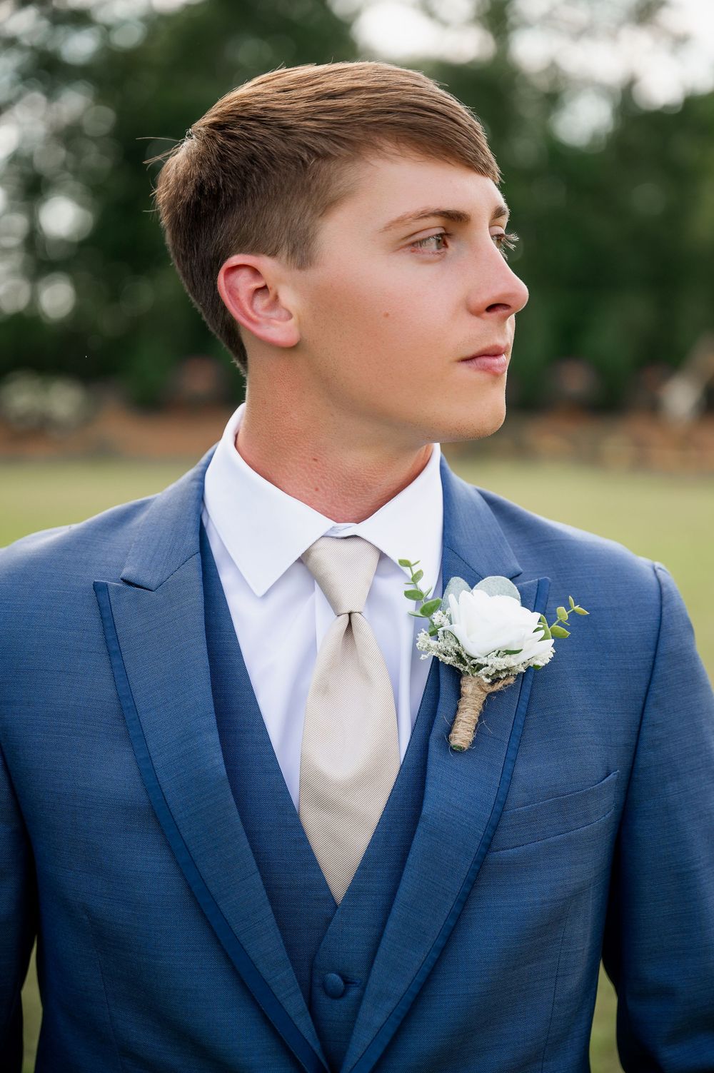 Profile view of groom in navy suit with white tie and boutonniere.