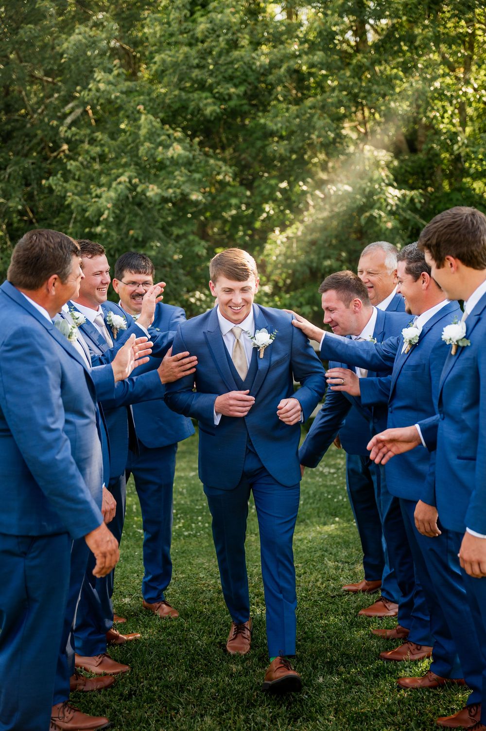 Wedding party in blue suits laughing together during outdoor photo session.