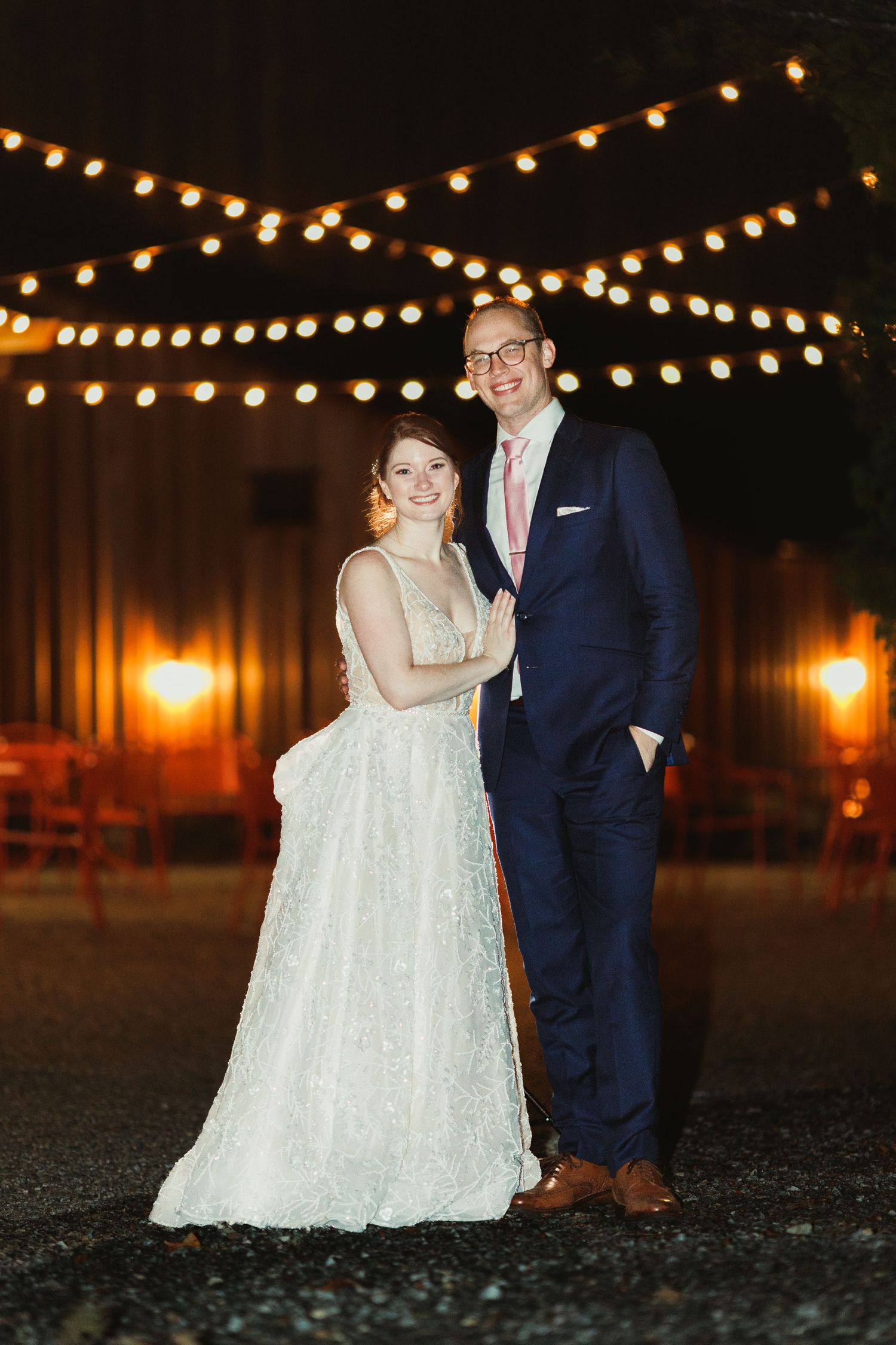 Romantic nighttime portrait under string lights at an outdoor wedding venue.