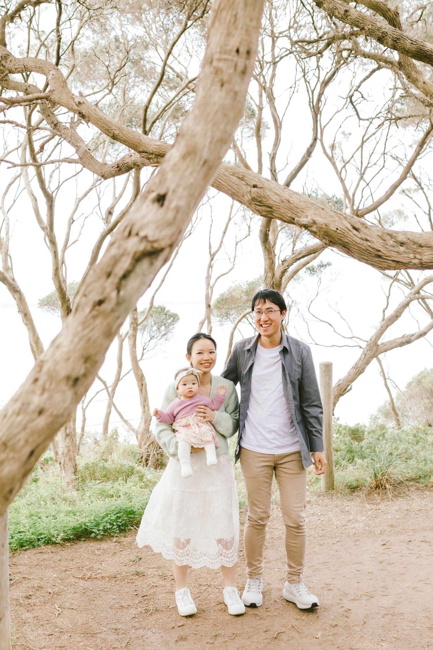 Family walking together on a dirt path surrounded by bare branched trees on a sunny day.