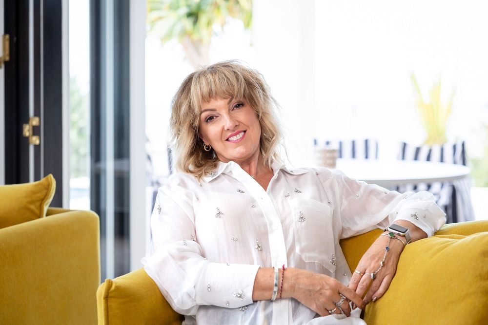 A person in a white button-down shirt sits and poses on a bright yellow accent chair in a modern interior setting.