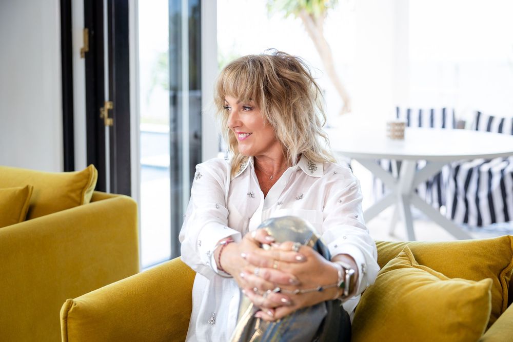 A person sits on a yellow couch in a bright modern space while holding a coffee mug.