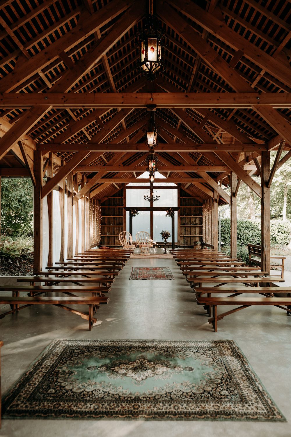 Rustic wooden chapel interior with rows of benches, exposed beams, hanging lanterns and a decorative rug down the aisle.