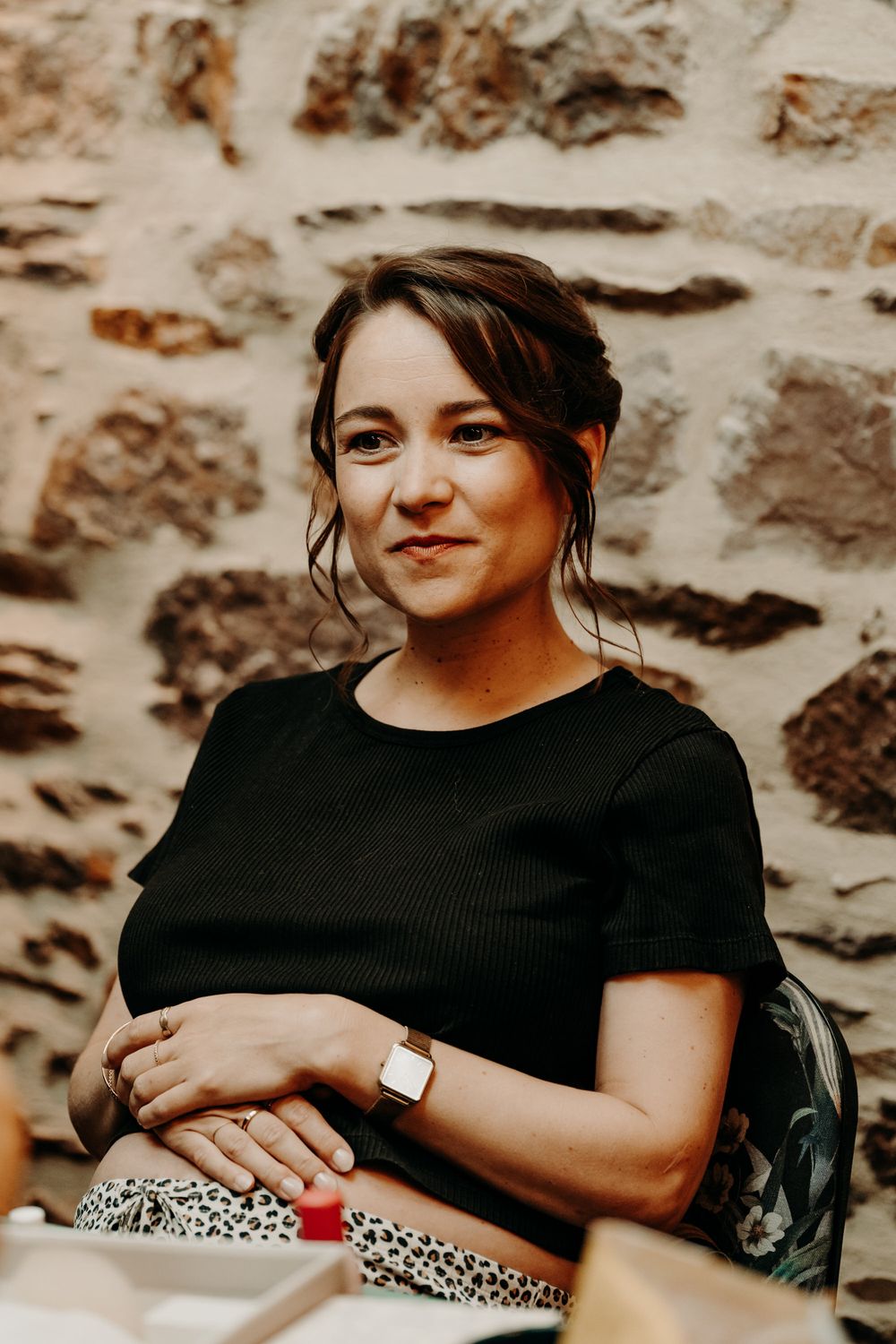 Person in black top sitting against stone wall in warm lighting.