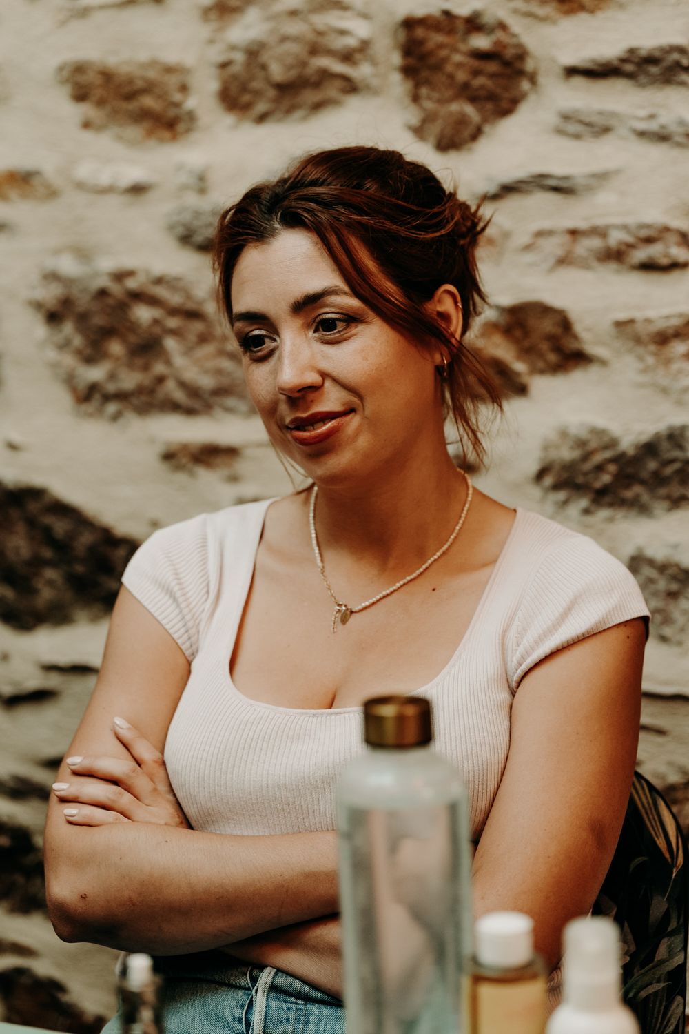 Person in white top sitting against textured stone wall with a drink nearby.