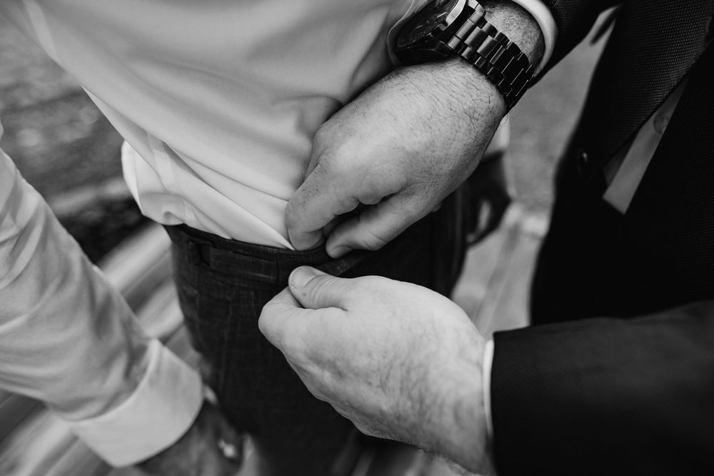 Black and white close-up of hands adjusting formal attire during wedding preparation.