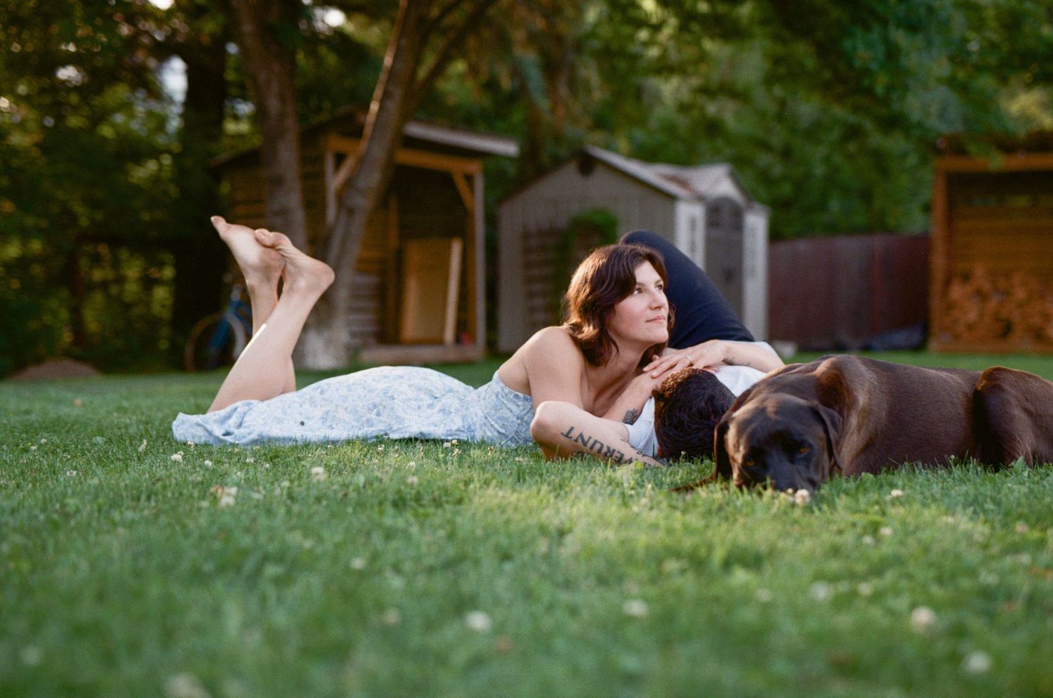 35 mm film photo of a woman laying on a man's chest in the grass, with their dog lying beside them in the evening light