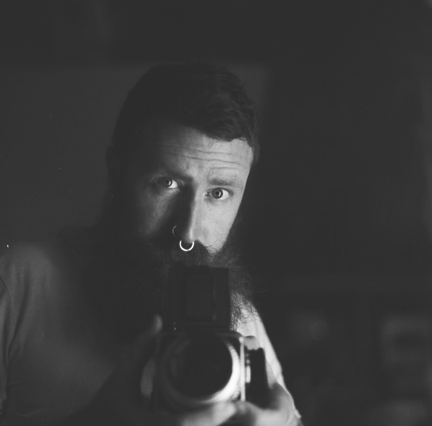 Dramatic black and white close-up portrait showing half of a person's face emerging from deep shadows.